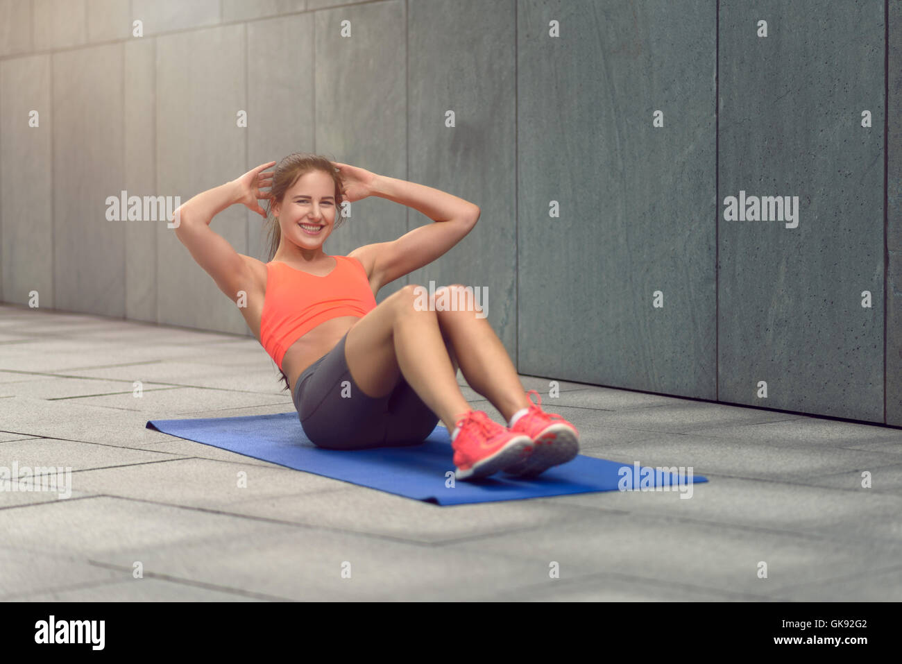 Sportliche junge Frau, die Arbeiten in den Hof eines Geschäftshauses auf ihrer Yoga-Matte dabei knirscht Stockfoto