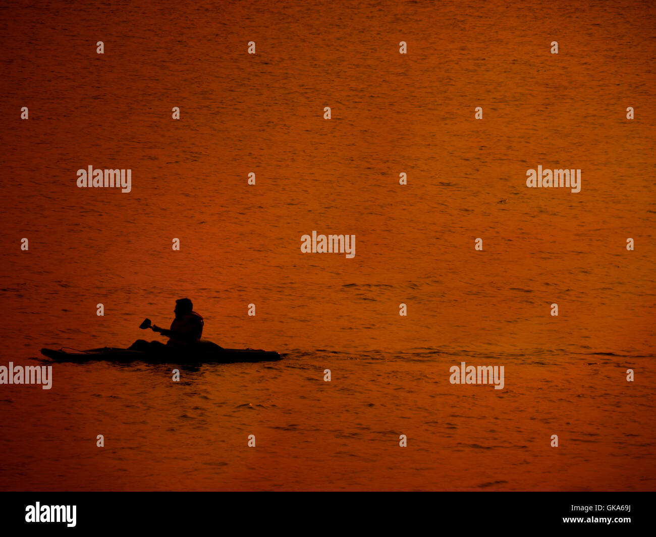 Eine Silhouette eines Mannes, der kayaking in einem See in seine Sommerferien im Abendlicht altrosa. Stockfoto