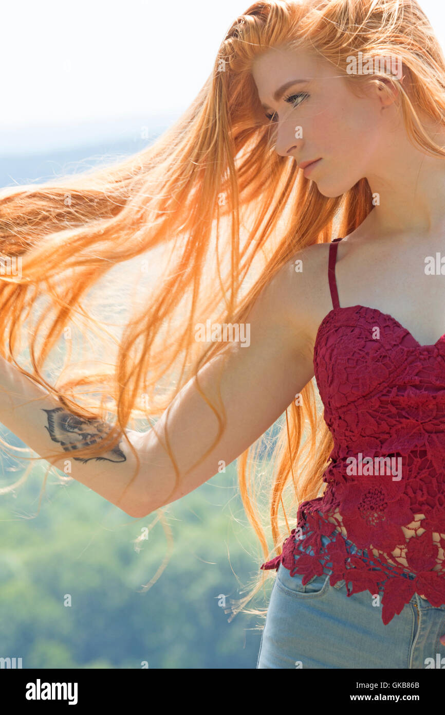 Schöne rote Kopf in rotes Top, halblängen am Berg stehend top mit goldenen Sonnenlicht durch ihr wallendes Haar. Stockfoto
