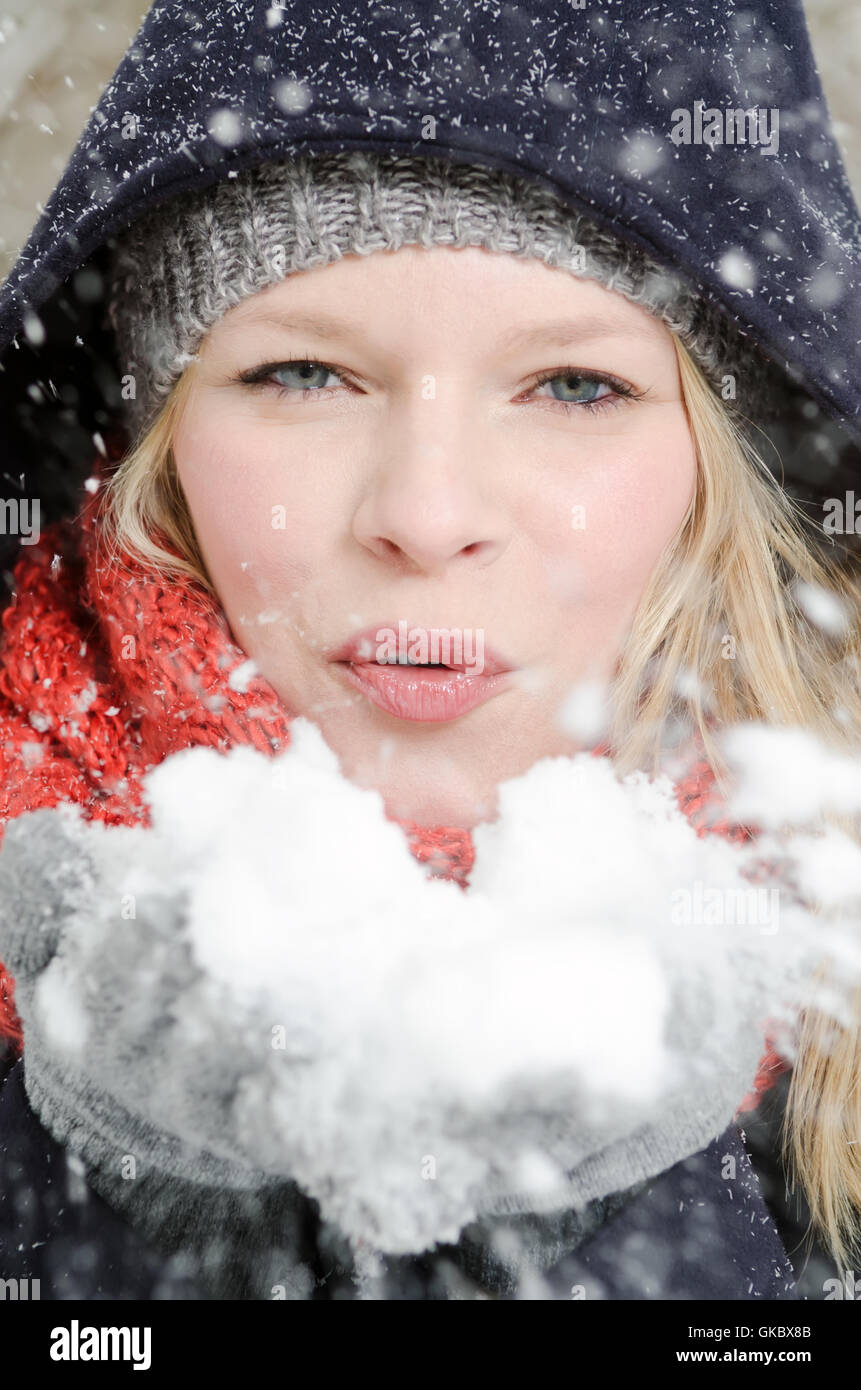 Junge, blonde Frau bläst in eine Handvoll Schnee Stockfoto