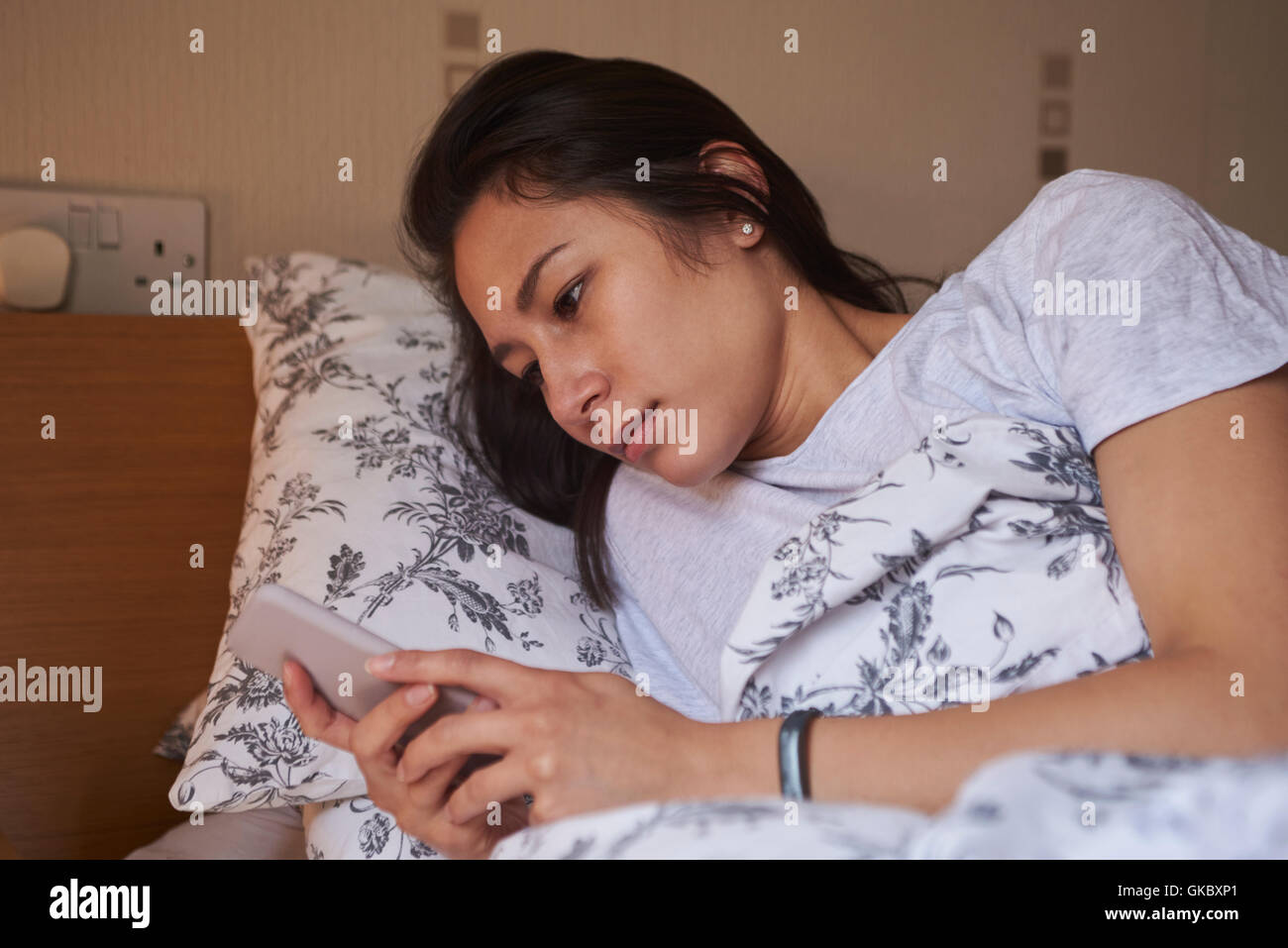Frau im Bett aufwachen und Überprüfung der Nachricht auf dem Handy Stockfoto
