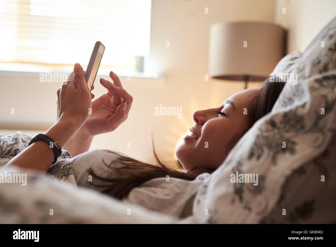 Frau im Bett aufwachen und Überprüfung der Nachricht auf dem Handy Stockfoto