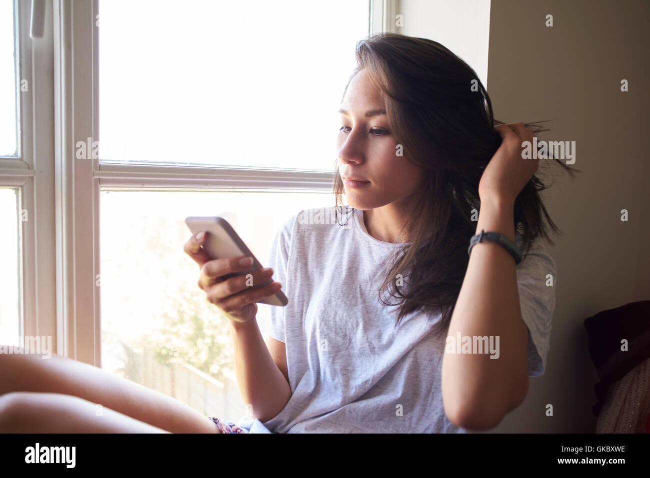 Frau Fenster sitzen und die Überprüfung der Nachricht auf dem Handy Stockfoto