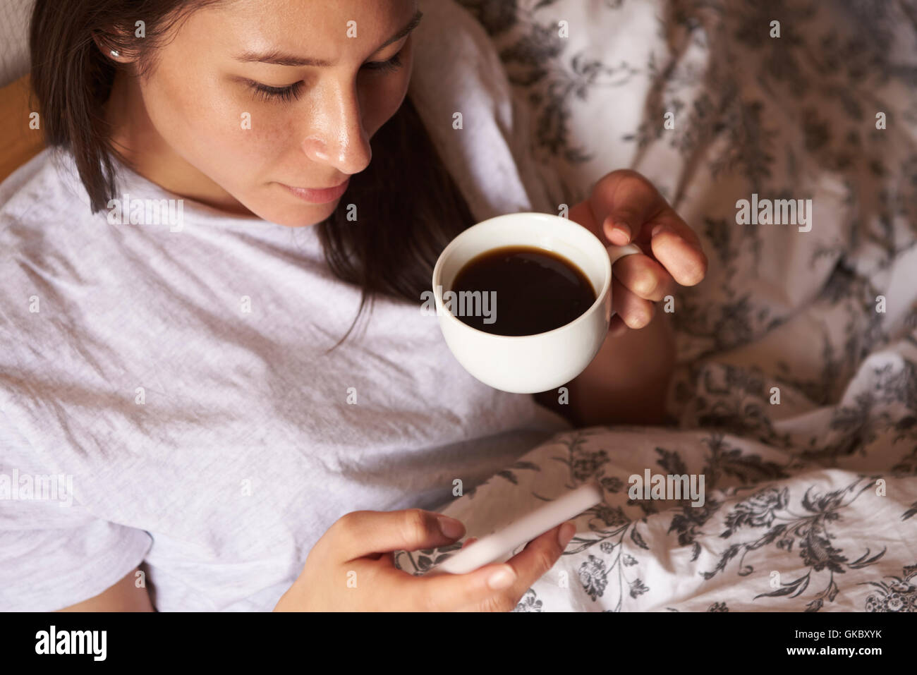 Frau mit Heißgetränk Check-Nachricht auf dem Handy im Bett Stockfoto