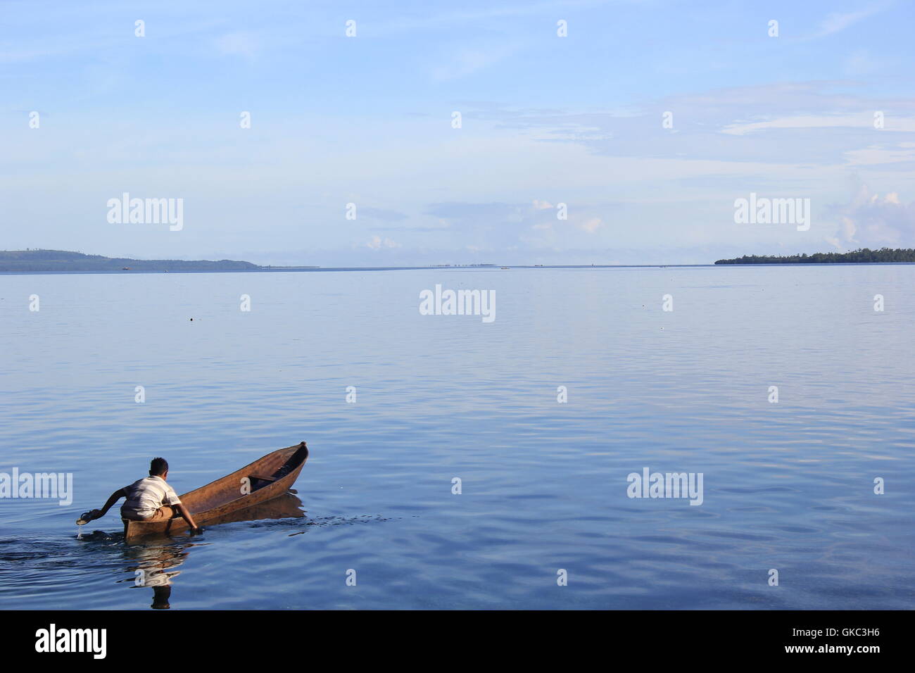 Ein kleiner Junge rudert sein kleines Boot mit seinen kleinen Händen auf einem ruhigen weiten offenen Meer. Das Foto wurde in Seram Island, Maluku Islands, Indonesien aufgenommen. Stockfoto
