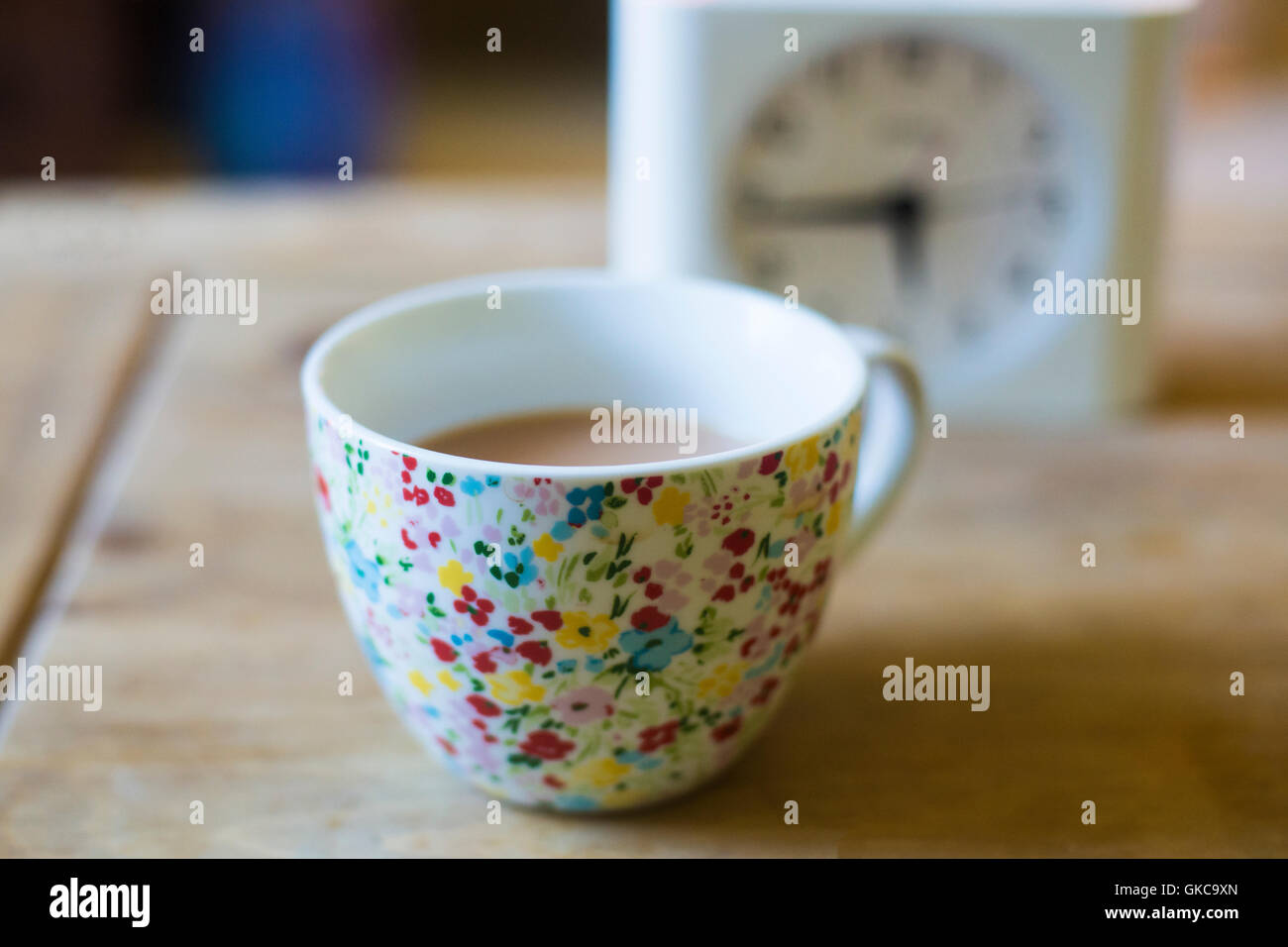 eine Tasse Tee auf einem Holztisch mit einer Uhr dahinter Stockfoto