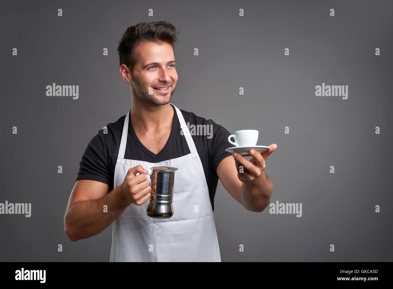 Ein junger Barista Mann lächelnd und halten eine Kaffeemaschine und eine Tasse Kaffee Stockfoto