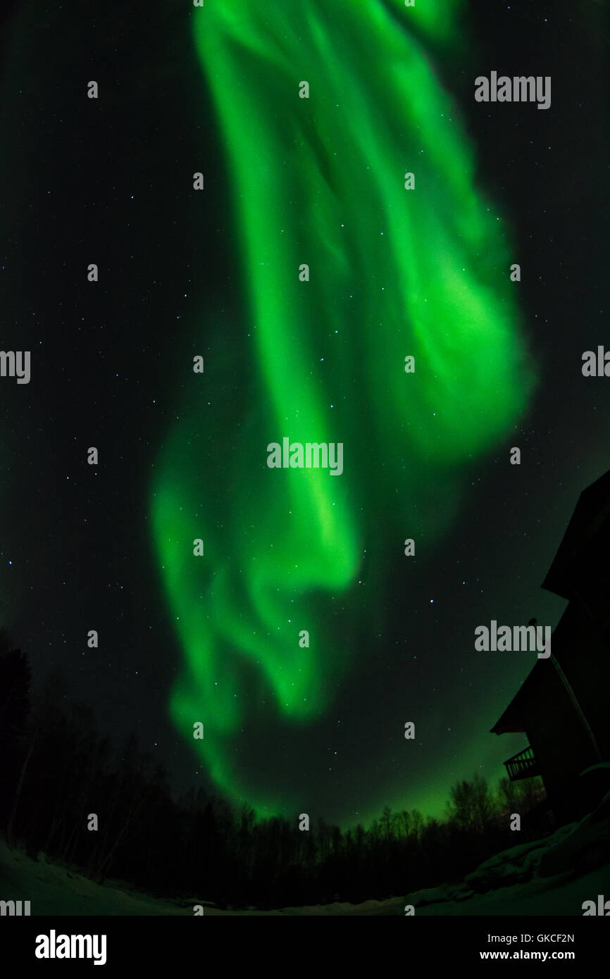 Eine grüne Aurora wirbelt über das Dach eines Hauses. Stockfoto