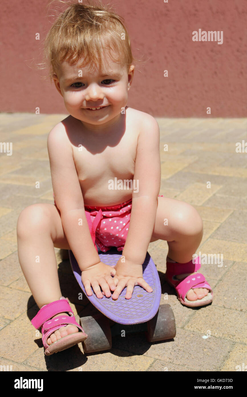 ein kleines Kind sitzt auf einem Skateboard shorts Sommer. vertikale Stockfoto
