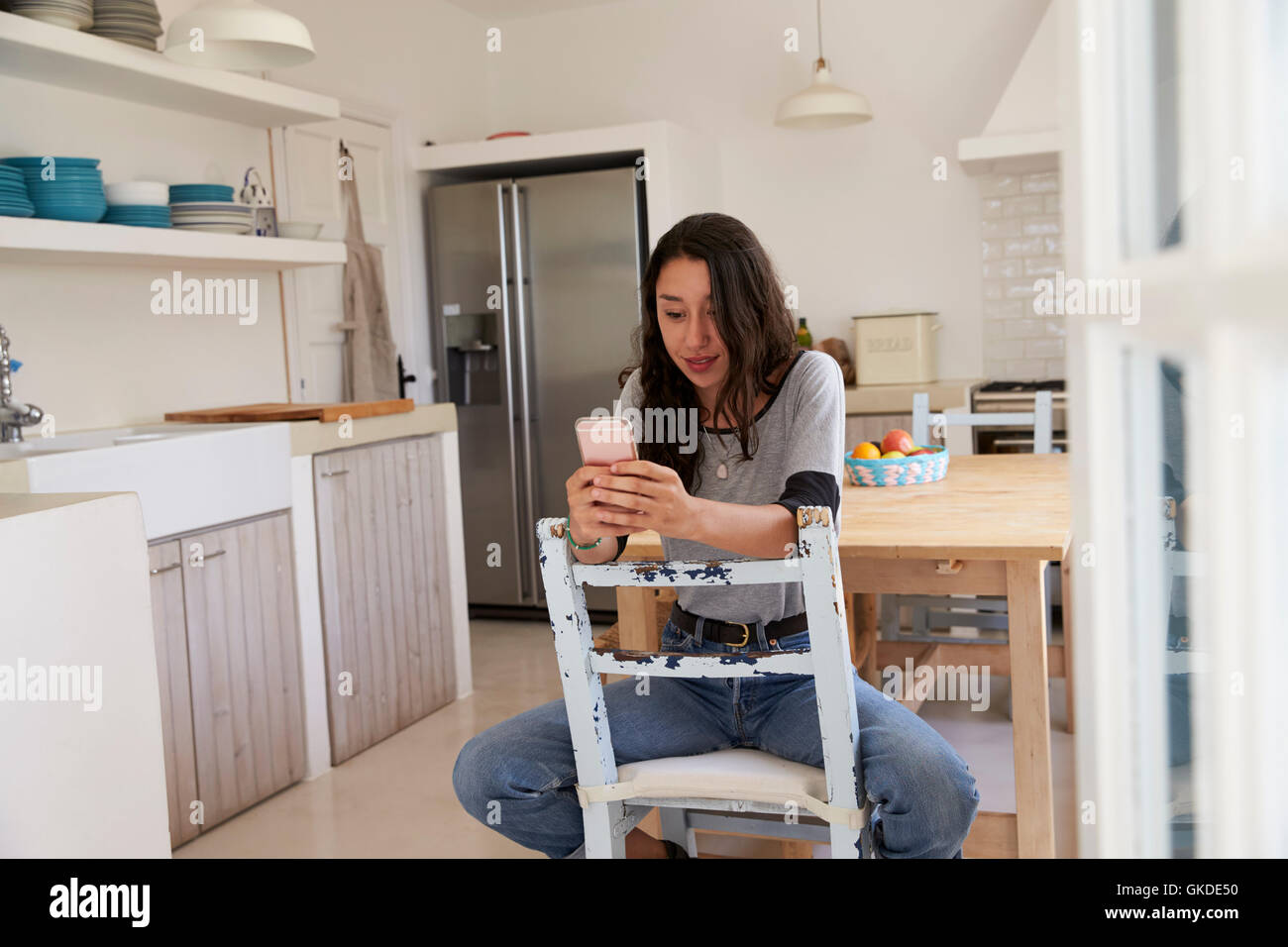 Teenager-Mädchen sitzen in der Küche mit Smartphone, Vorderansicht Stockfoto