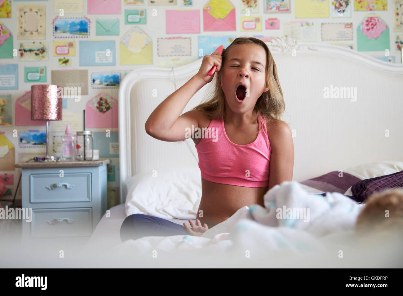 Junges Mädchen sitzt auf Bett und Bürsten Haare während Gähnen Stockfoto