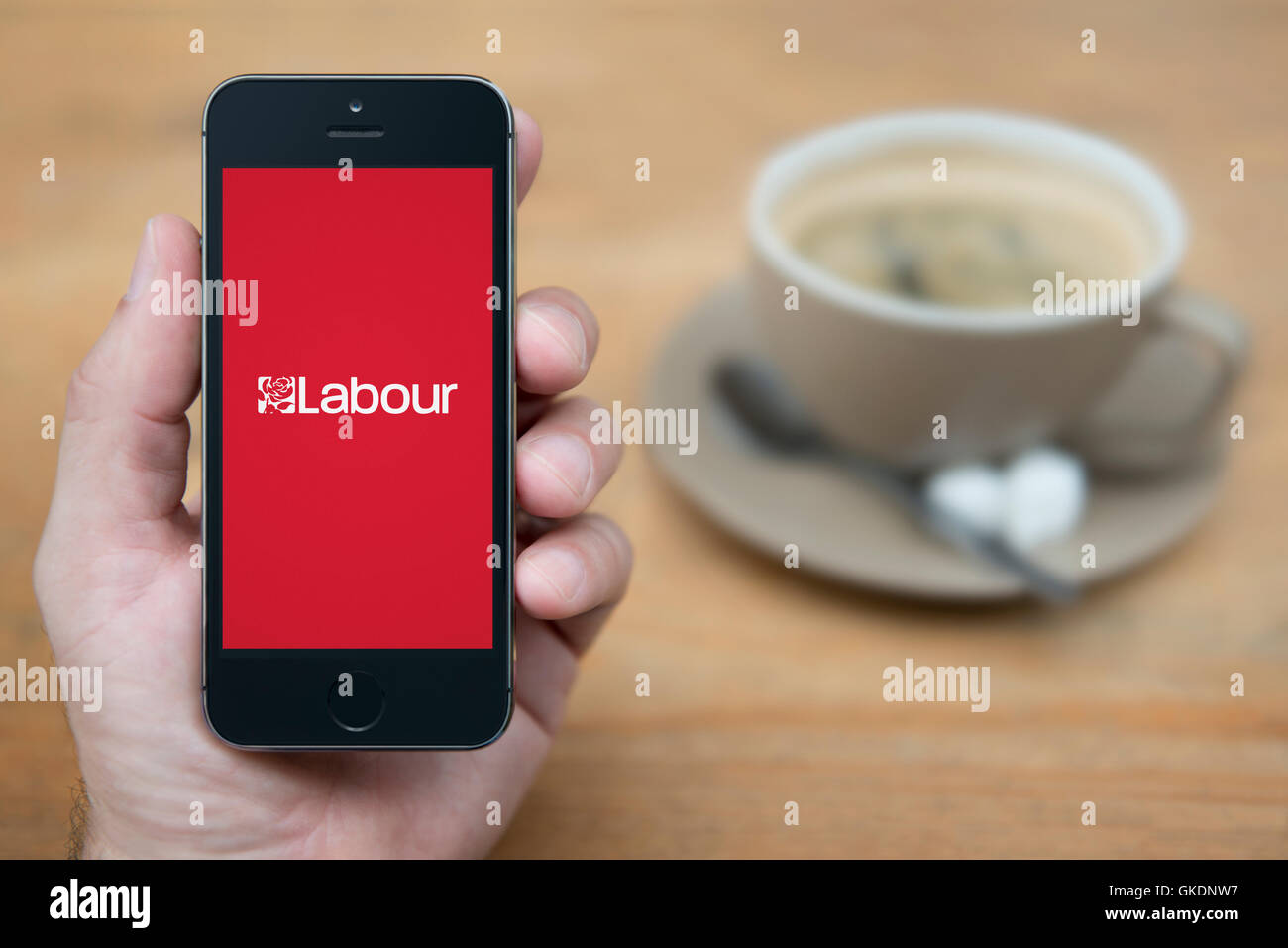 Ein Mann schaut auf seinem iPhone die Labour-Partei-Logo anzeigt, während setzte sich mit einer Tasse Kaffee (nur zur redaktionellen Verwendung). Stockfoto