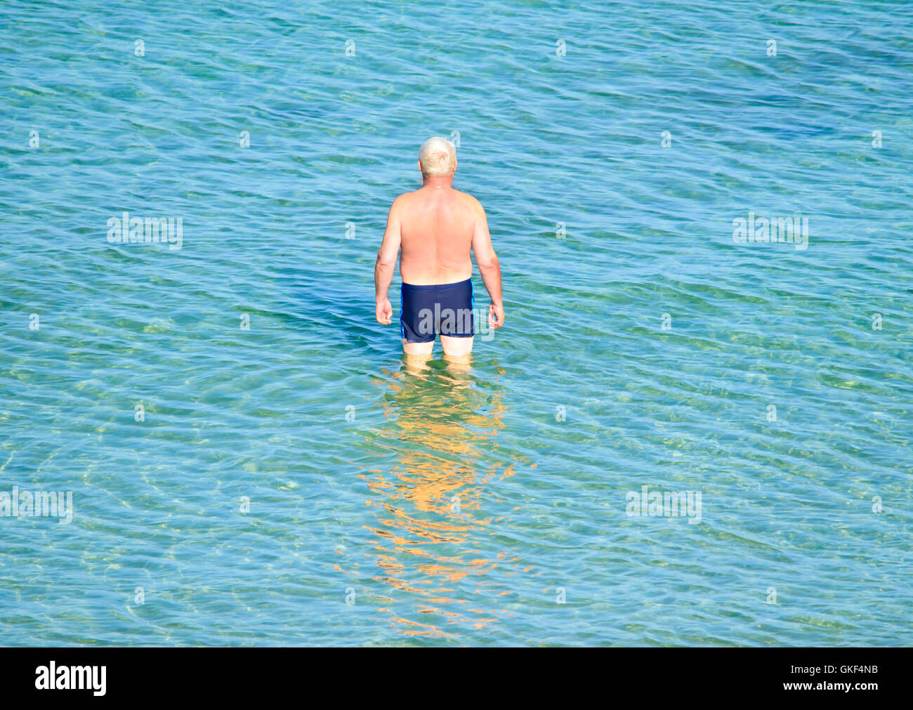 älterer Mann stehen knietief im klaren Meerwasser Stockfoto