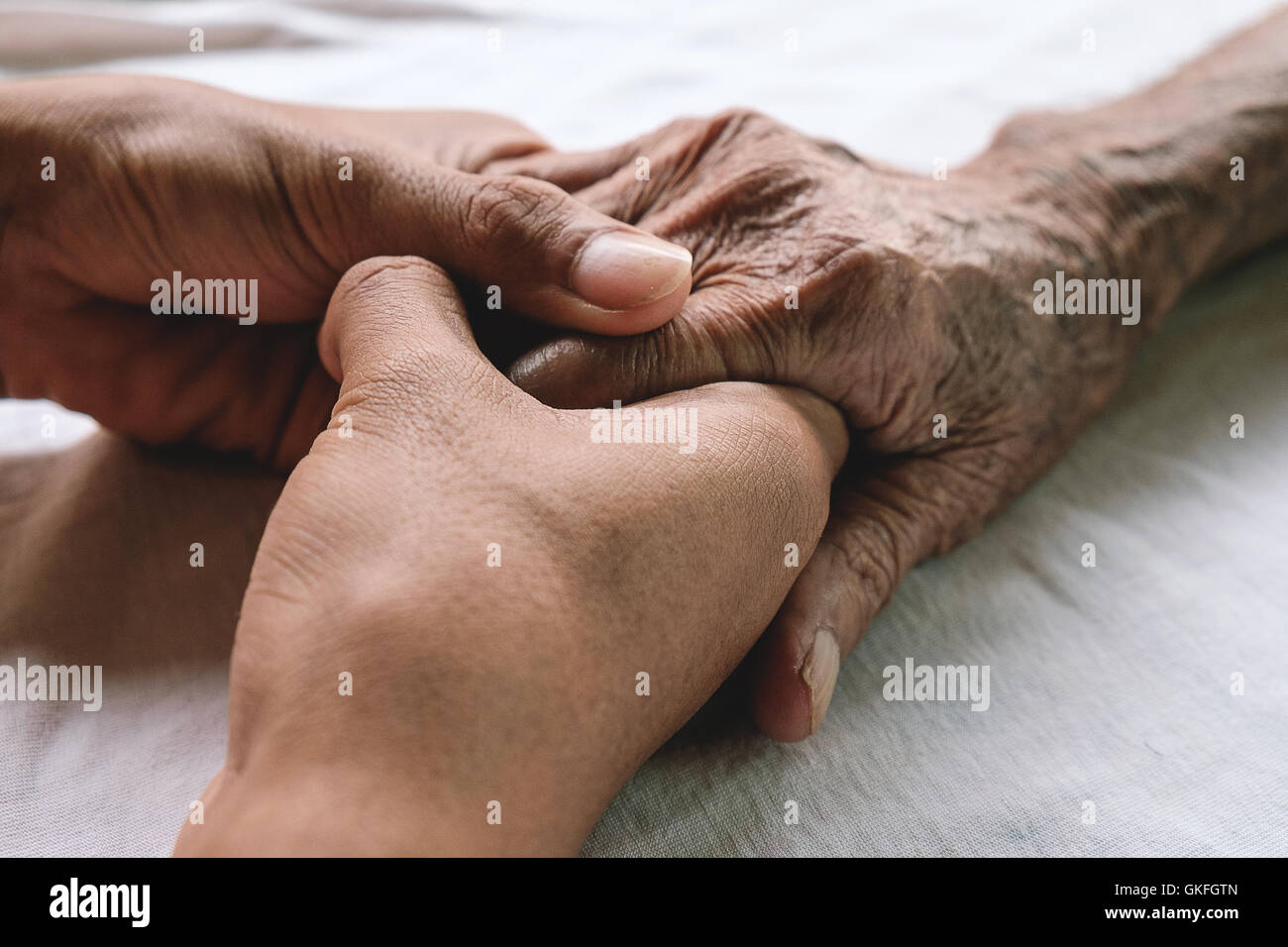 Hände von dem alten Mann und ein junger Mann auf einem weißen Bett in einem Krankenhaus. Stockfoto