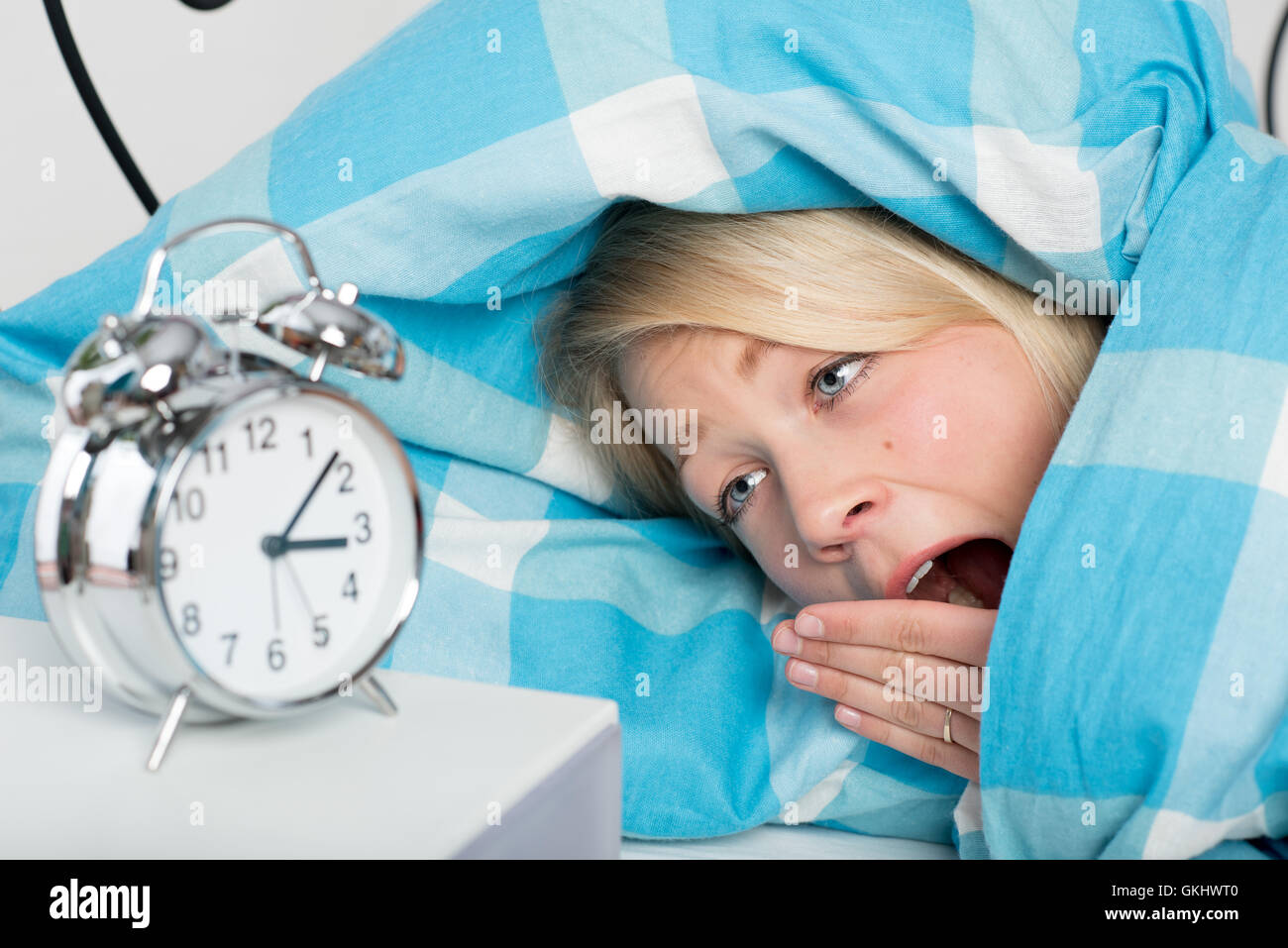 junge Frau schlaflos im Bett liegen und Blick auf die Uhr Stockfoto