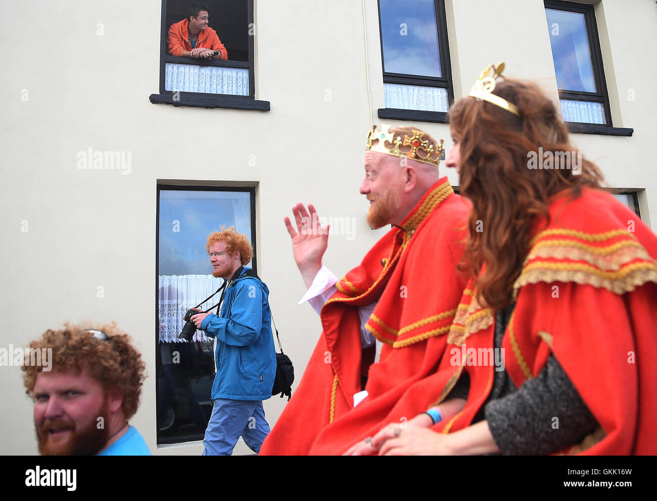 Ein Mann wacht aus einem Fenster im oberen Stock als frisch gekrönter "König und Königin der rothaarige" Alan O'Neill und Emma Ni Chearuil führen die Parade auf der irischen Rothaarige Convention in dem Dorf Crosshaven in Cork, Irland statt. Stockfoto
