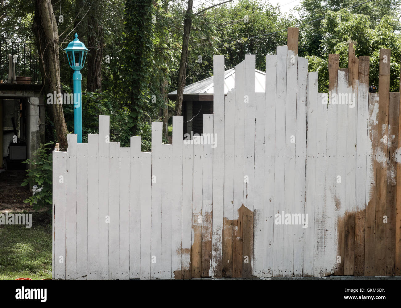 Unebene Platten in einem Zaun sind teilweise getüncht, mit einem Laternenpfahl und Garten auf der Rückseite Stockfoto