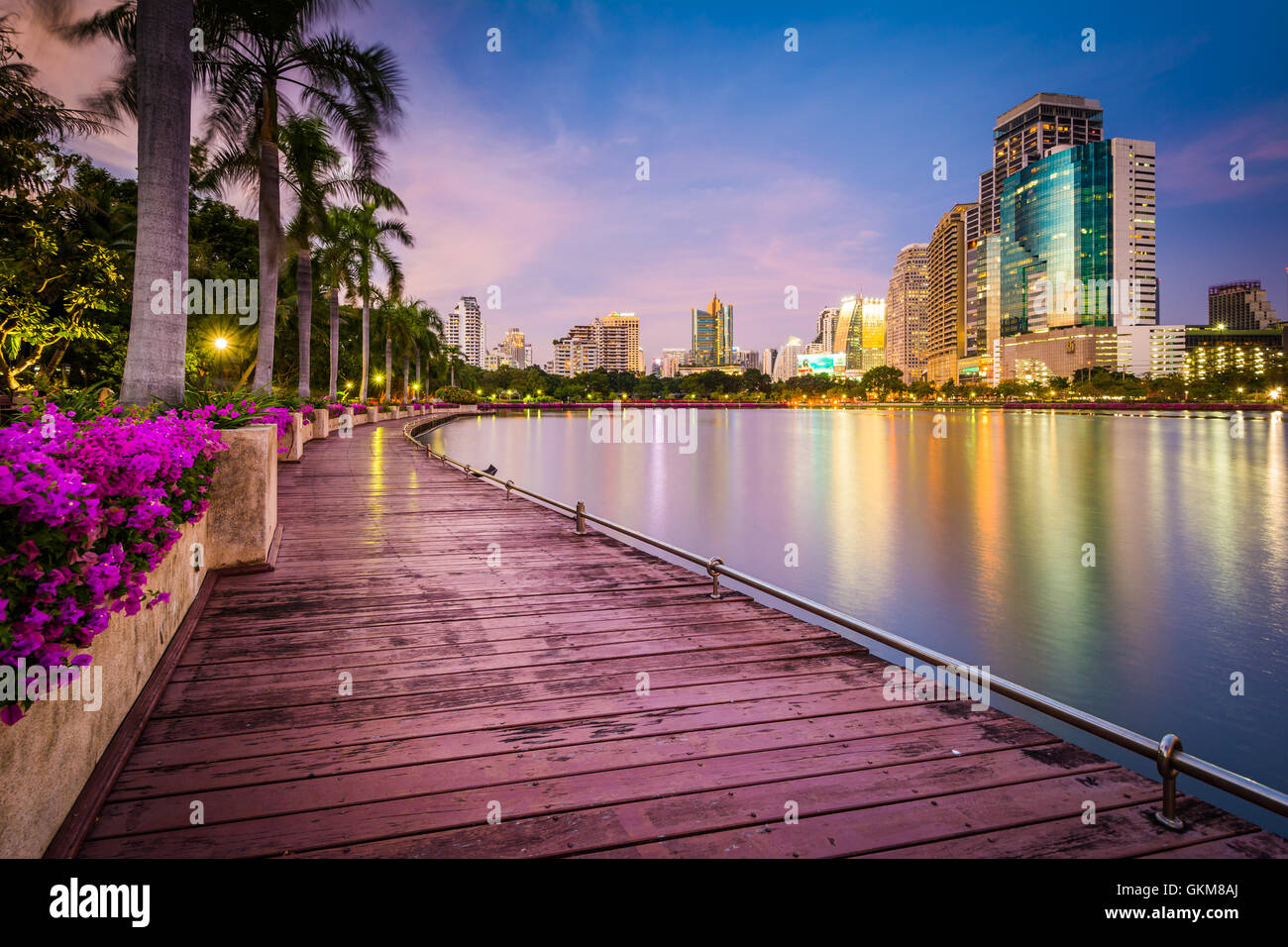 Moderne Wolkenkratzer, Blumen und Palmen entlang Lake Rajada bei Sonnenuntergang im Benjakiti Park in Bangkok, Thailand. Stockfoto
