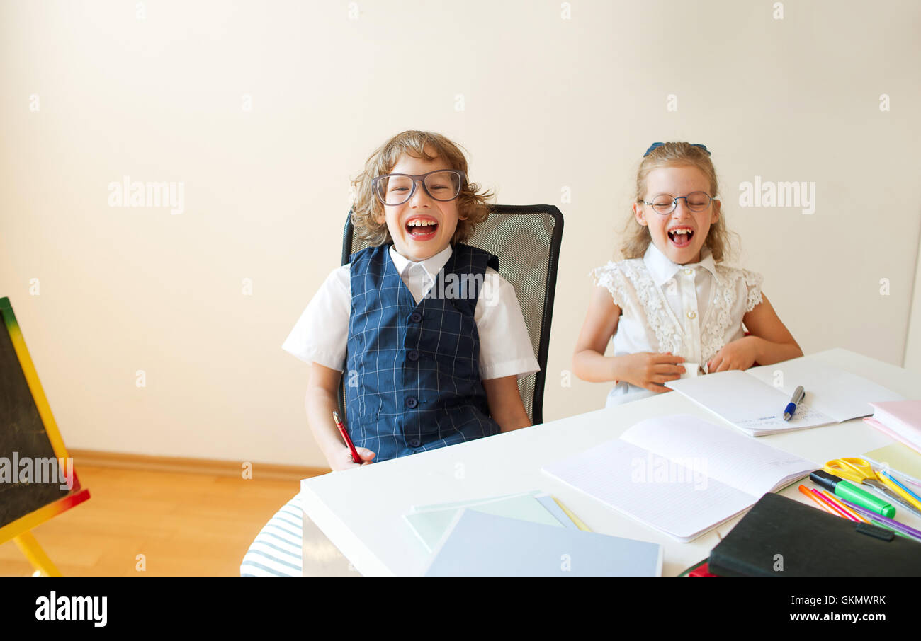 Teilen Sie lächerlich wenig Studenten bebrillten, jungen und Mädchen, die gleichen Schreibtisch. Sie sind Schüler einer Grundschule. Sie lachen. Stockfoto