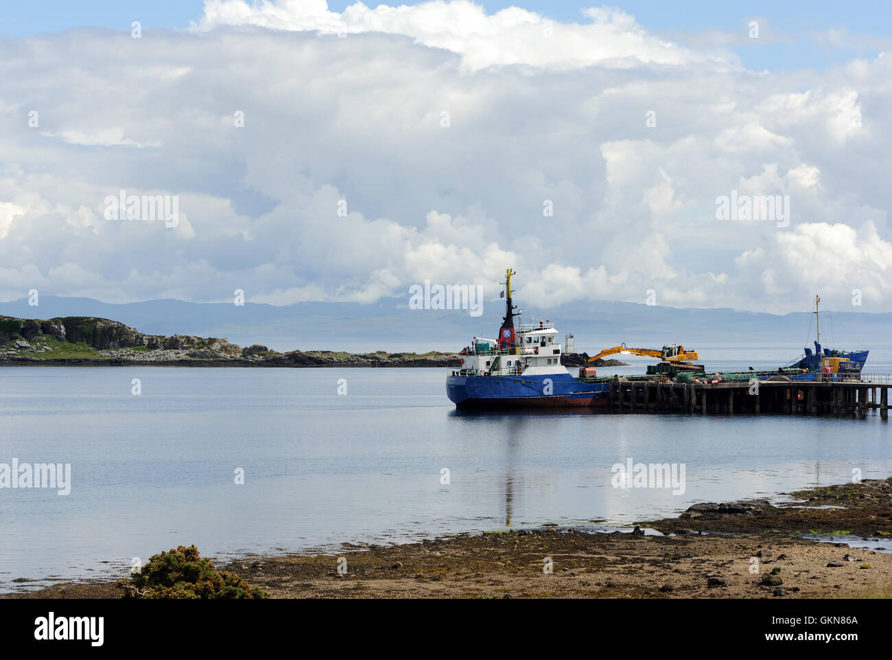 Ein Frachtschiff und an einem Kai in einem geschützten Hafen auf einem noch Sommertag. , Islay, Innere Hebriden, Argyll, Schottland, Großbritannien. Stockfoto