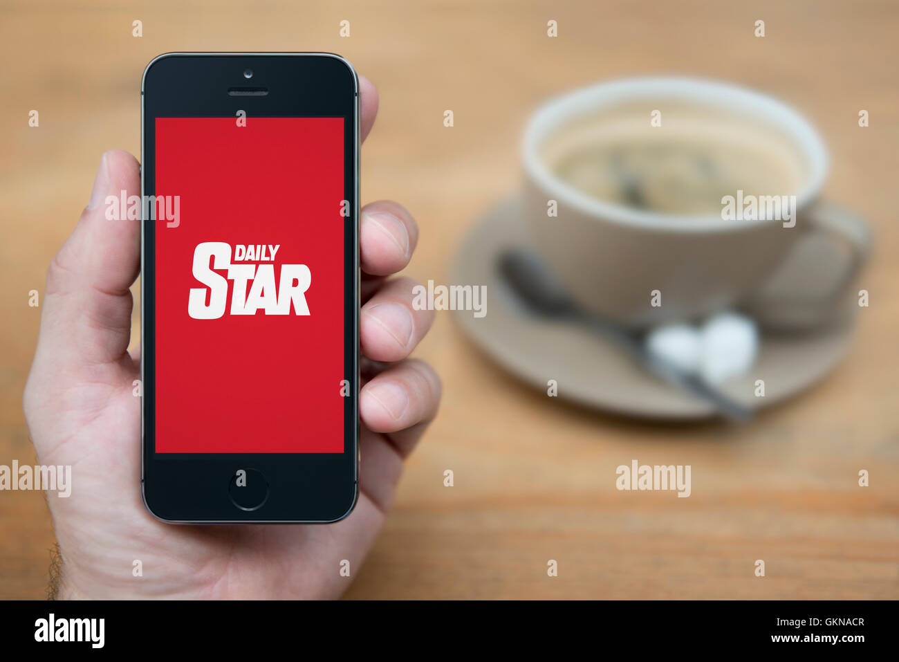 Ein Mann schaut auf seinem iPhone die Daily Star-Logo anzeigt, während bei einer Tasse Kaffee (nur zur redaktionellen Verwendung) saß. Stockfoto