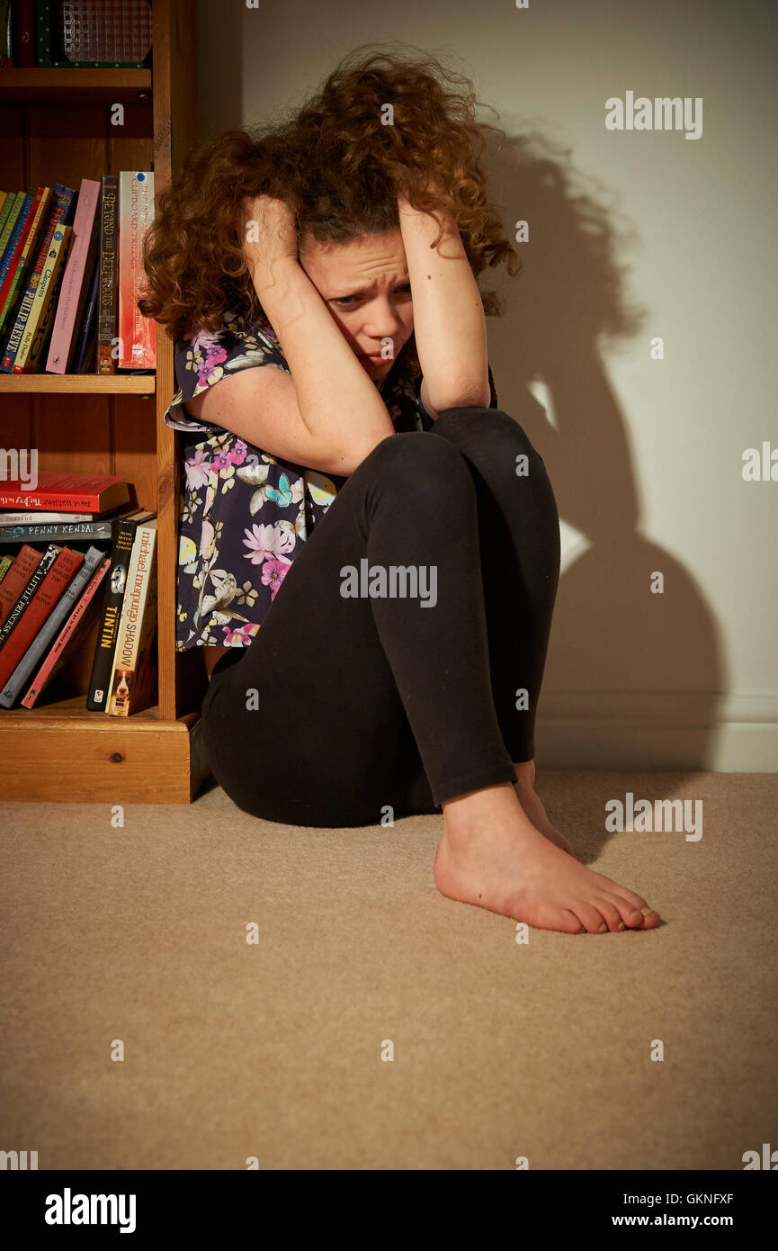 Kind verärgert und allein sitzen auf dem Boden neben einem Bücherregal in ihrem Schlafzimmer. Stockfoto