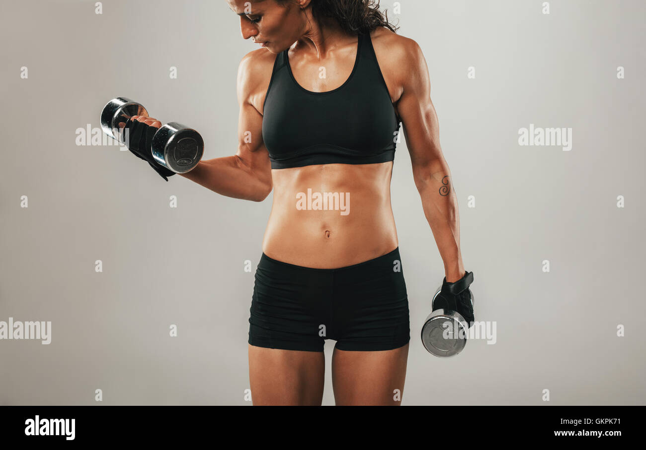 Einzelne schöne sportliche junge Erwachsenfrau im Zentrum des grauen Hintergrund heben von Gewichten Stockfoto