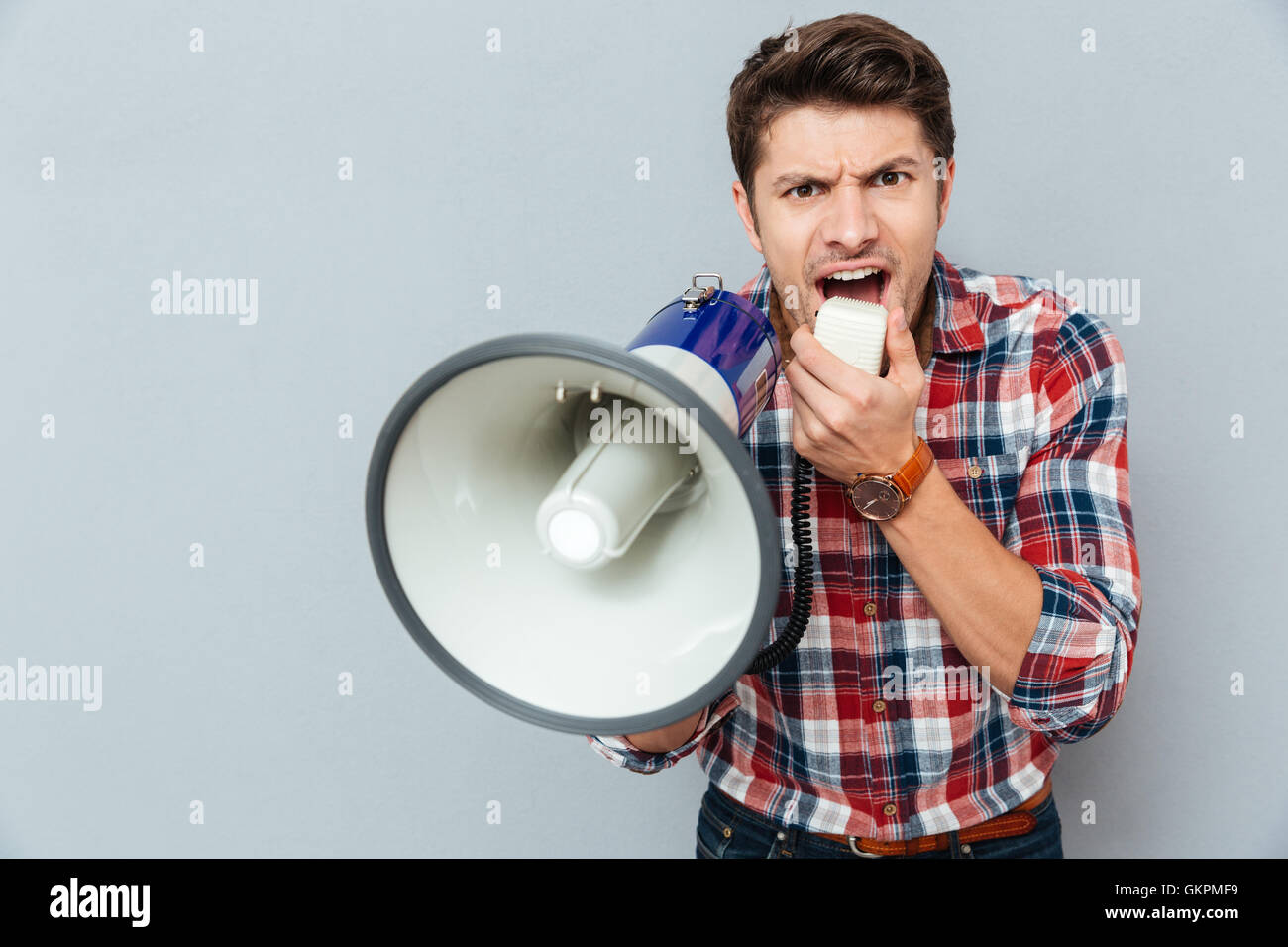 Verrückt verrückt junger Mann im karierten kurzen schreien in Megaphon auf grauem Hintergrund Stockfoto