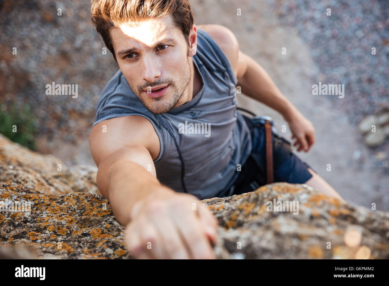 Mann für einen Griff zu erreichen, während er Felsen klettert auf einem steilen Felsen Stockfoto
