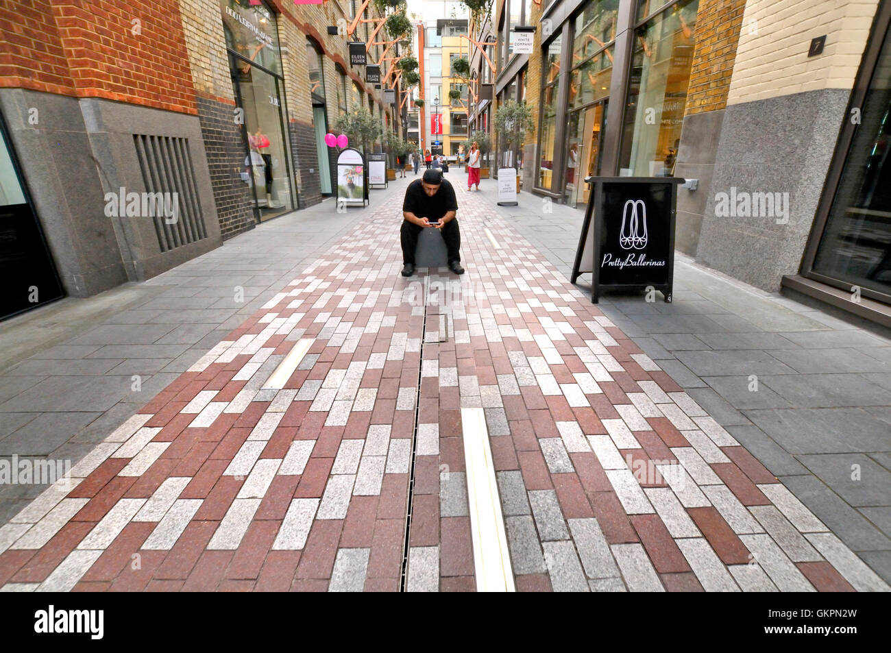 London England, UK. Mann mit seinem Handy, sitzt allein in einer Straße Stockfoto