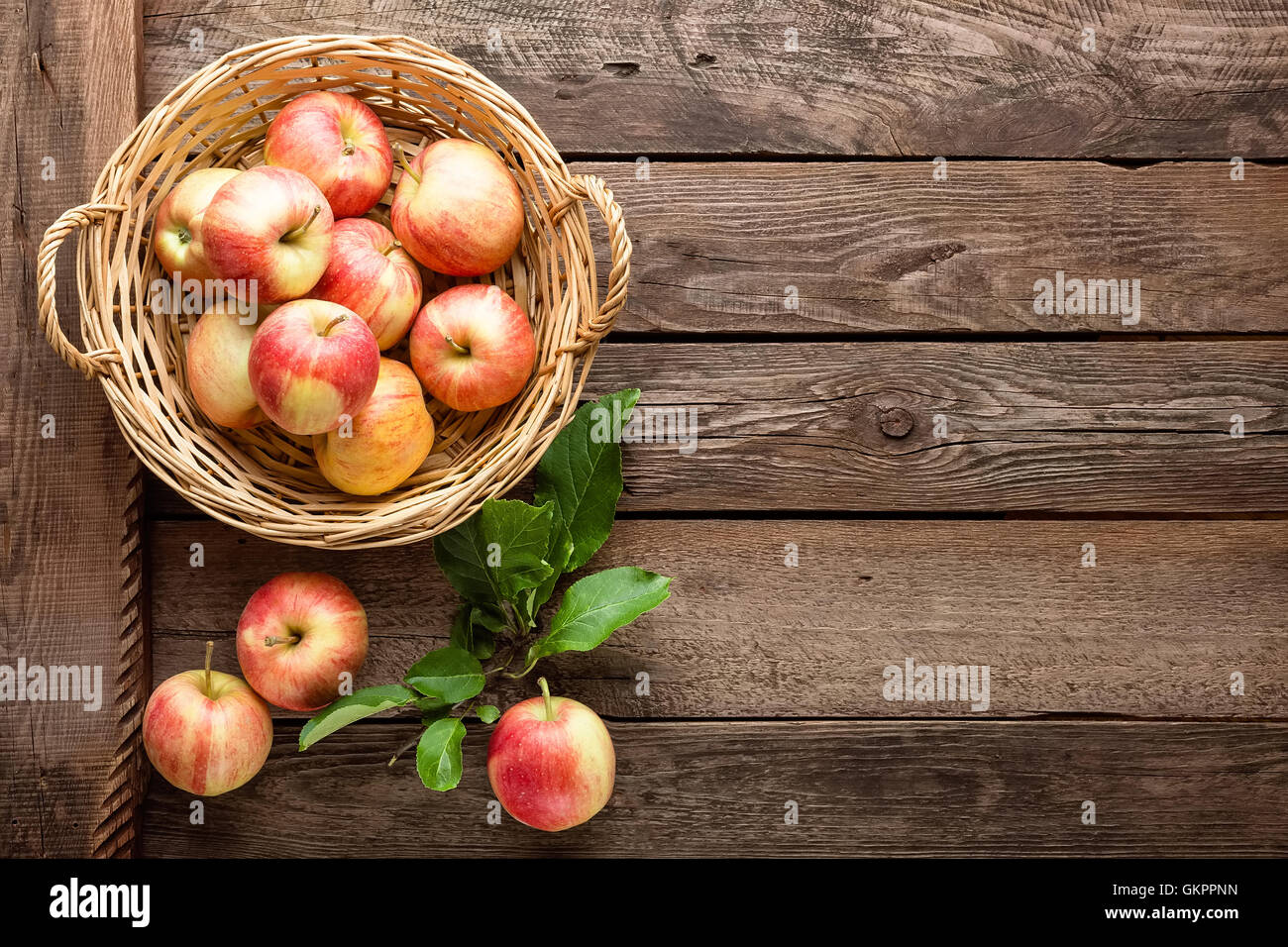 frische rote Äpfel im Weidenkorb auf Holztisch Stockfoto