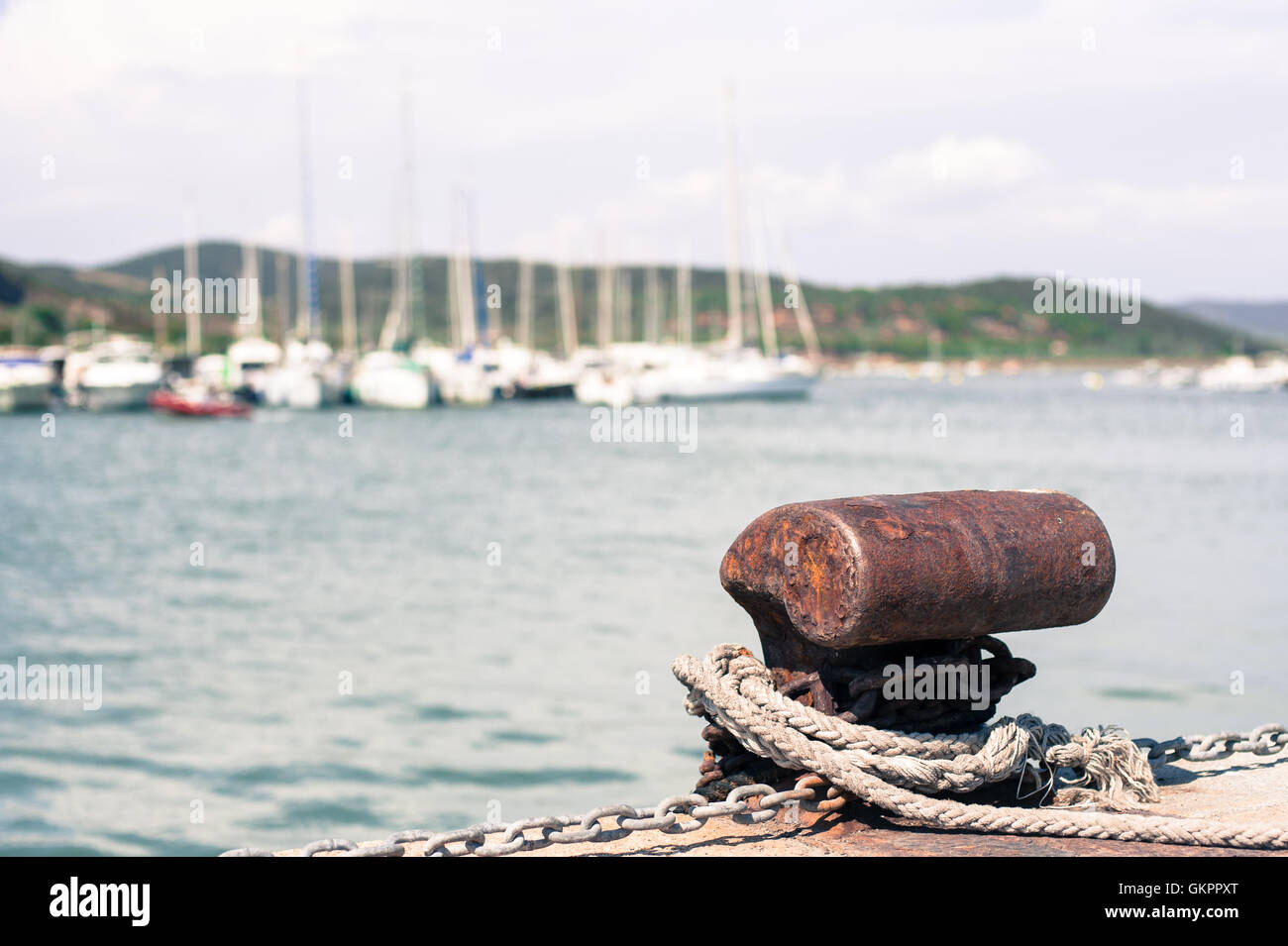 Verrostete Festmacher Poller im Dock von Hafen-Pier, Seil und Segelboot im Hintergrund unscharf Stockfoto