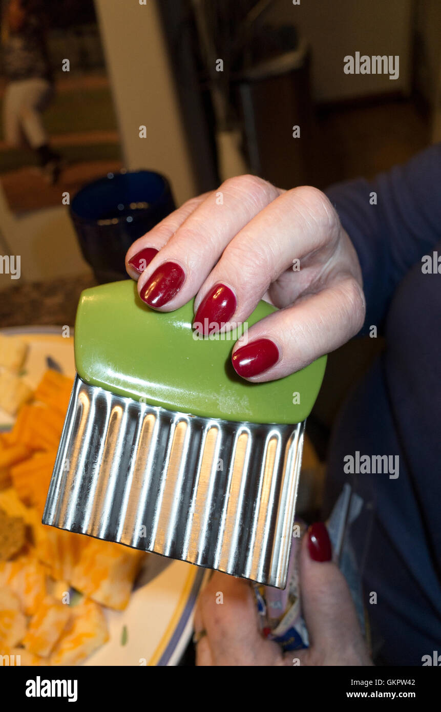 Frau mit rot lackierten Nägeln einen gezackten Käse-Schredder mit grünem Griff hält. St Paul Minnesota MN USA Stockfoto