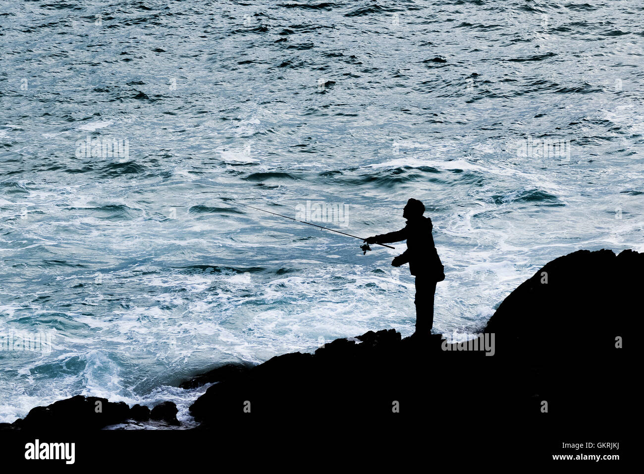 Die Silhouette eines Mannes Angeln vom Felsen in Newquay, Cornwall. Stockfoto