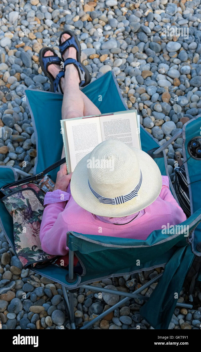 Ältere weibliche Person Buch sitzen am Kiesstrand Stockfoto