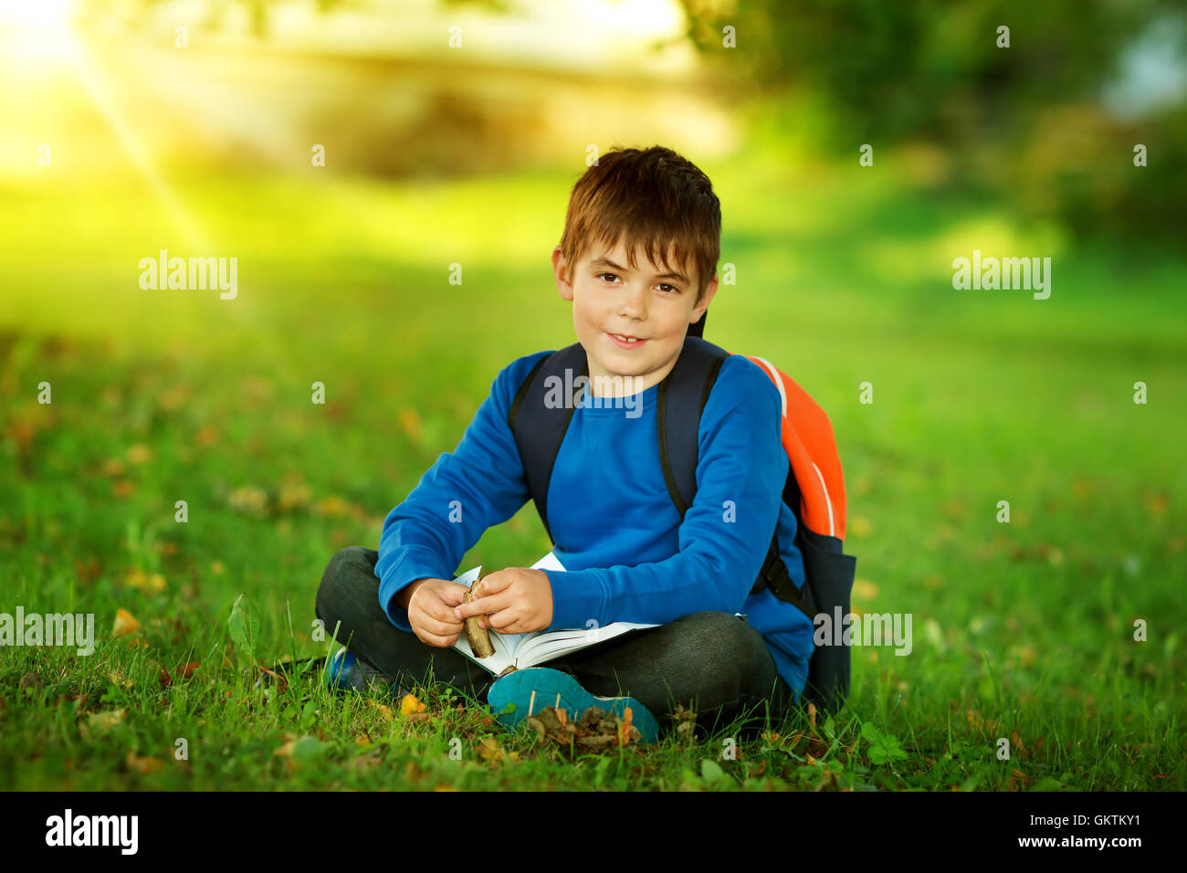 Junge sitzt mit Rucksack im park Stockfoto