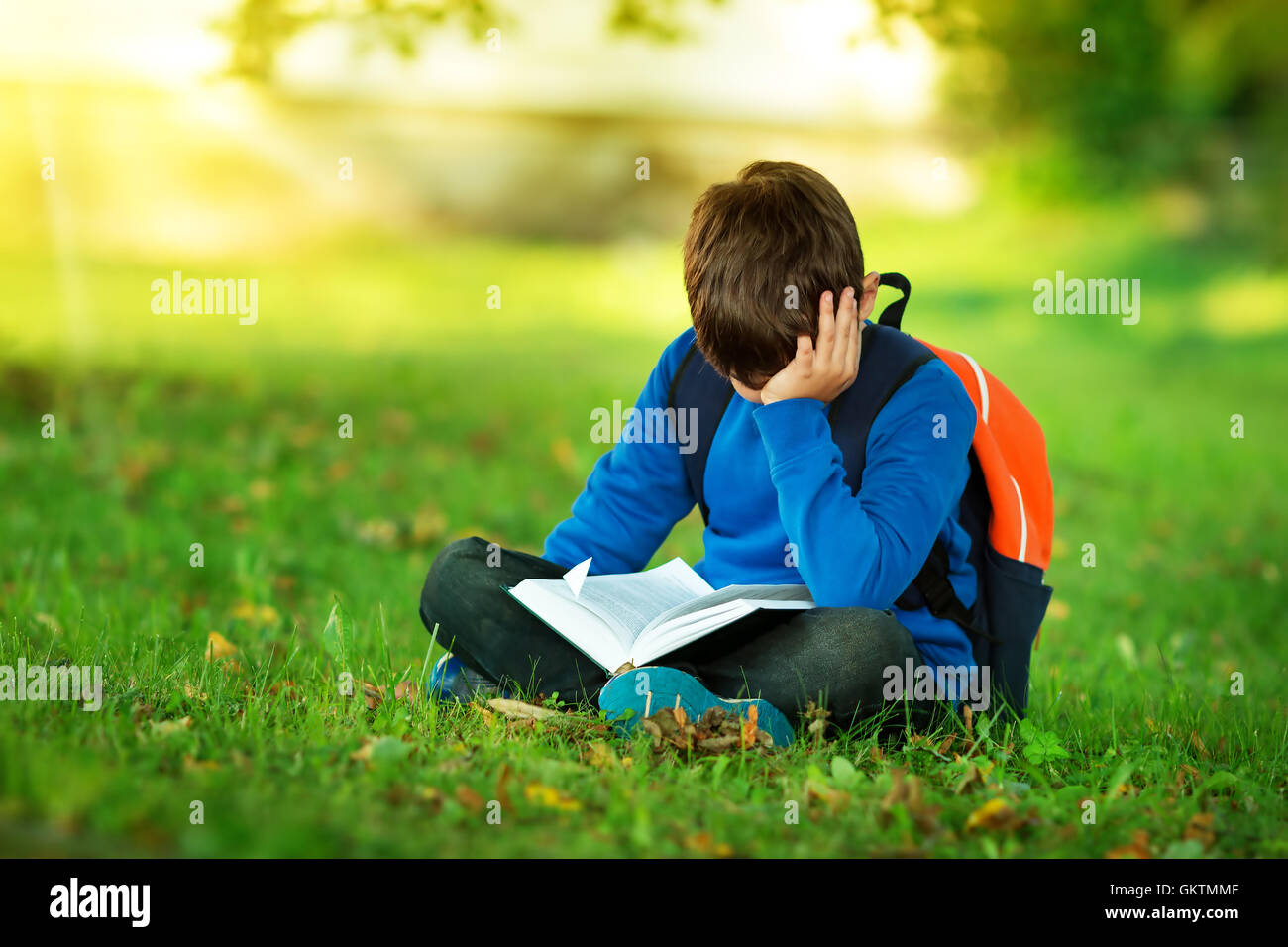 Junge sitzt mit Rucksack im park Stockfoto