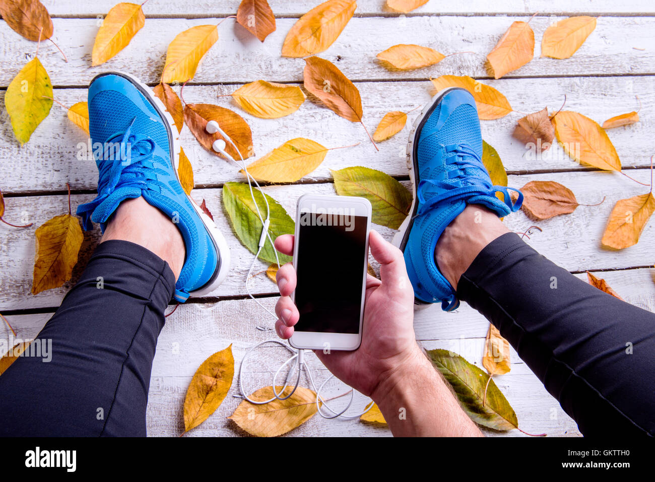Läufer in Sportschuhen. Smartphone und Kopfhörer. Blätter im Herbst. Stockfoto