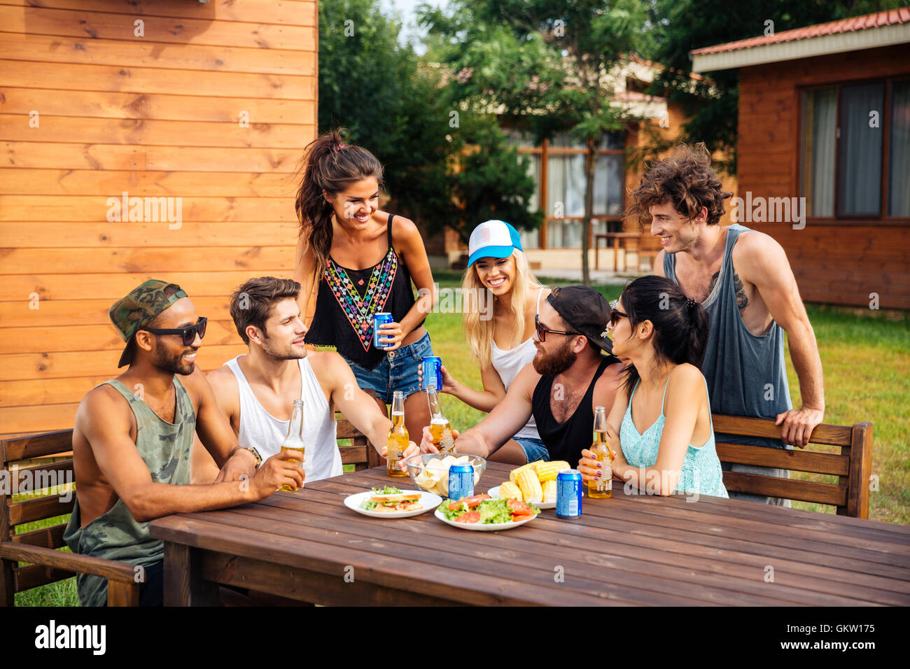 Glückliche Gruppe befreundeter Teenager sitzen am Tisch, trinken Bier und Snacks zu essen Stockfoto