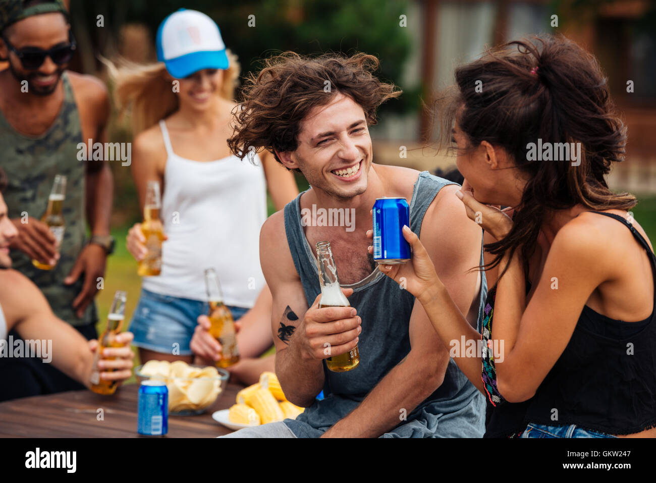 Glückliche Gruppe befreundeter Teenager sitzen am Tisch, trinken Bier und Spaß im freien Stockfoto