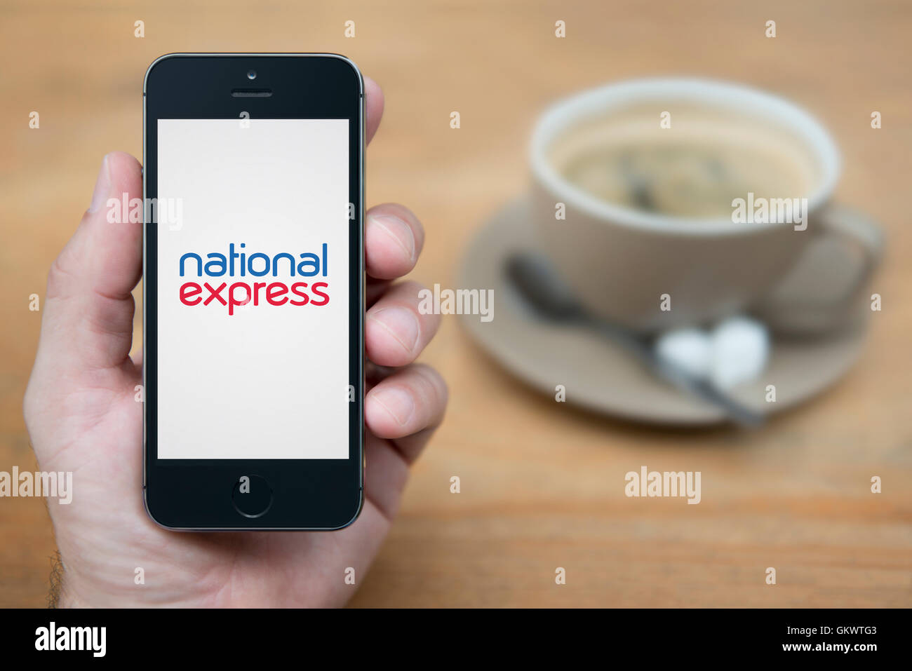 Ein Mann schaut auf seinem iPhone die National Express-Logo anzeigt, während bei einer Tasse Kaffee (nur zur redaktionellen Verwendung) saß. Stockfoto