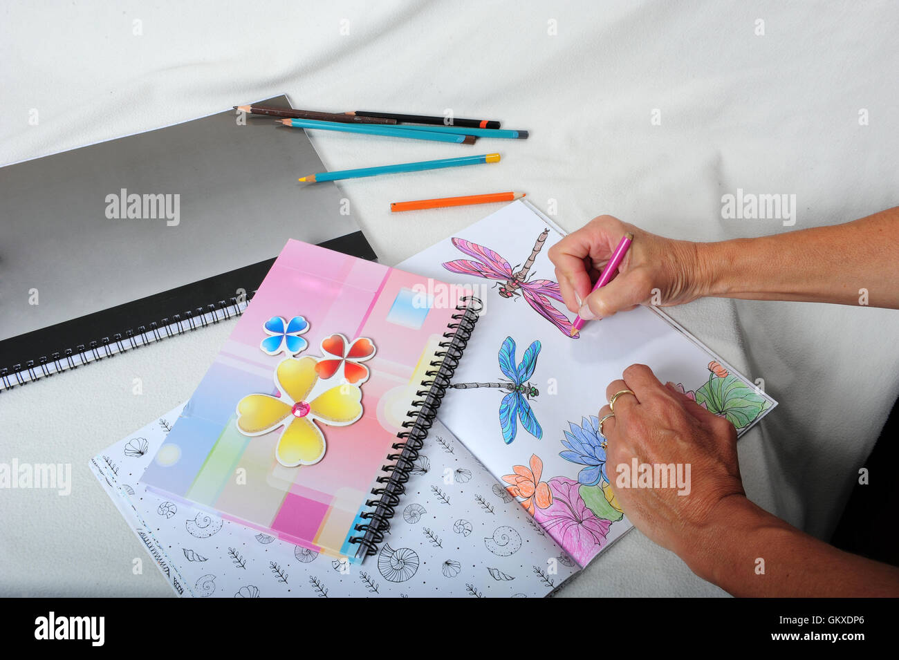 Die Hände der erwachsenen Frau. Malvorlagen in Malbuch. Stifte und Notizbücher auf Tisch herumliegen. Stockfoto