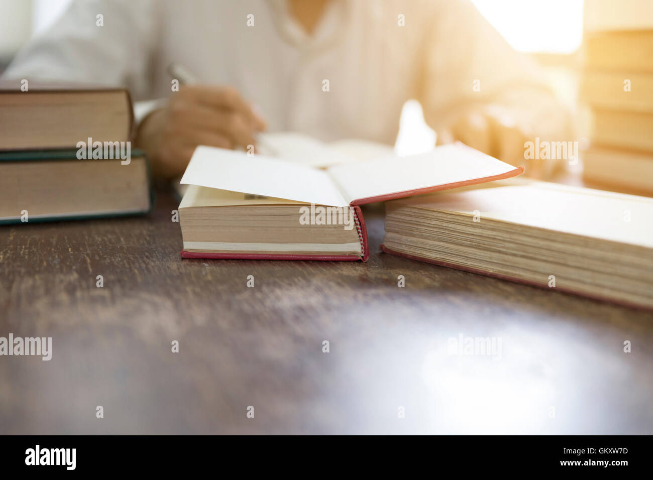 Mann liest Buch mit Lehrbuch Stack auf hölzernen Schreibtisch in der Bibliothek Stockfoto