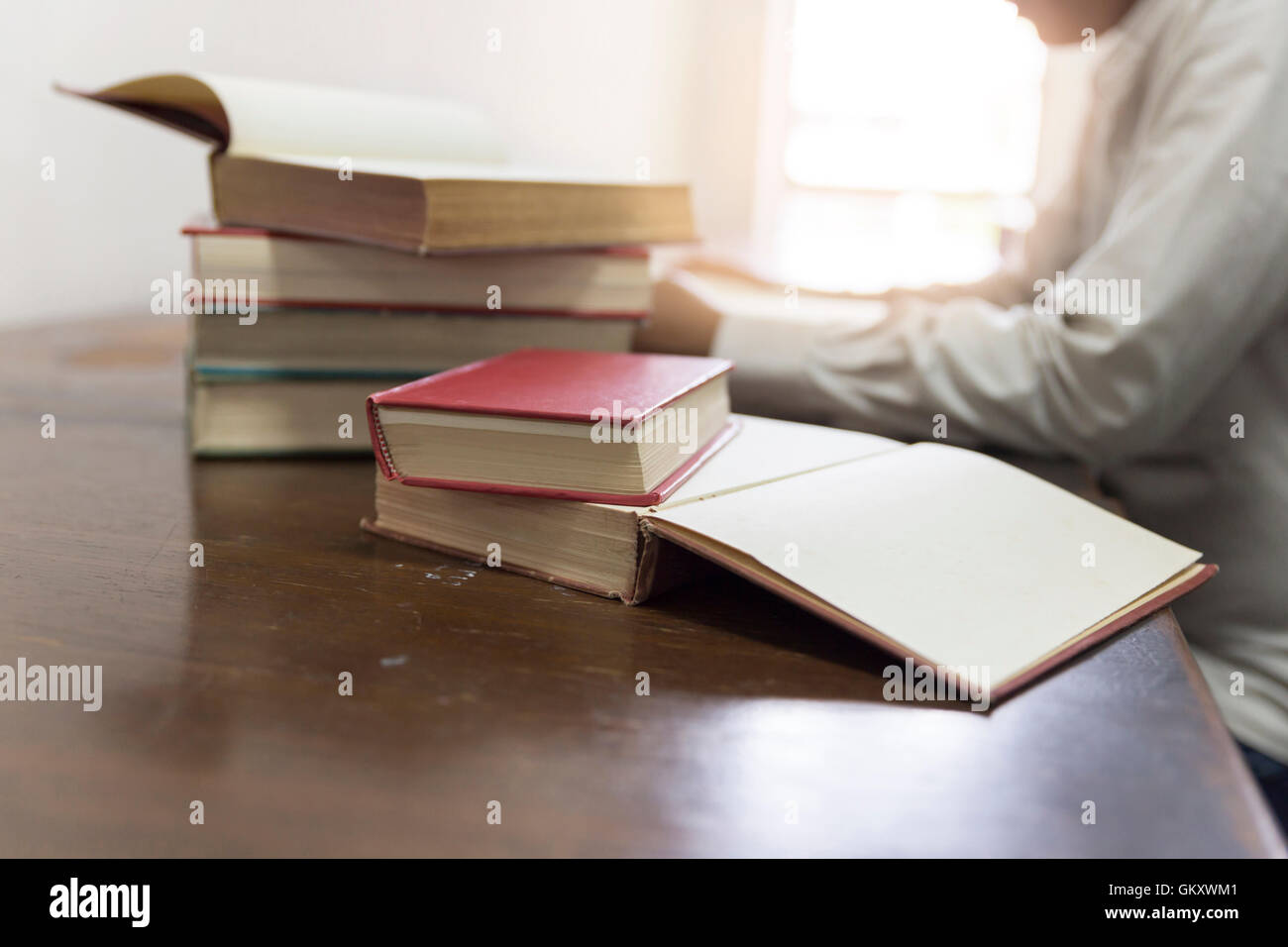 Mann liest Buch mit Lehrbuch Stack auf hölzernen Schreibtisch in der Bibliothek Stockfoto