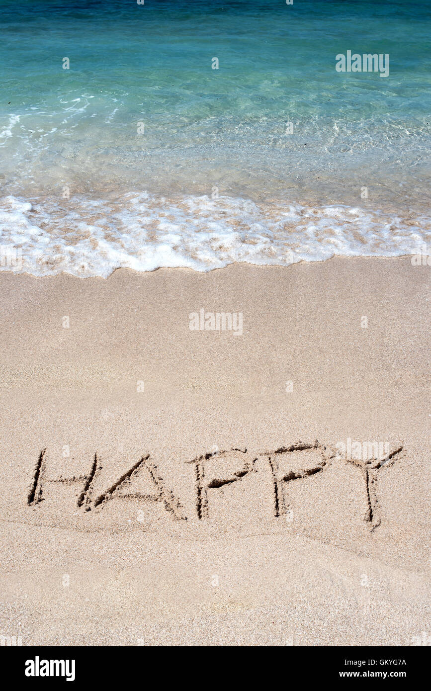 Das Wort Happy gezeichnet auf einem tropischen Strand am Rande der eine sanfte Brandung und blaues Meer Stockfoto