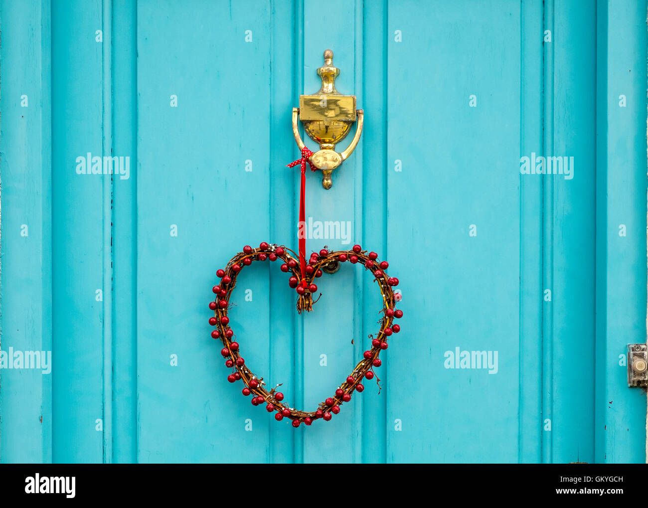 Eine herzförmige Kranz hängen eine Türkis farbigen Tür aus einer Messing-Klopfer Stockfoto