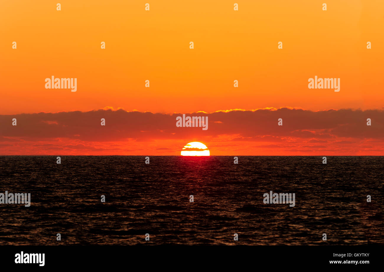 Ocean Sunset ist eine weiße heiße Sonnenuntergang am Meer Horizont unter einer Schicht von Wolken in strahlend orange sunset Himmel. Stockfoto