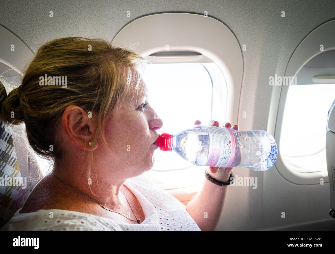 Eine Frau trinkt eine Flasche Wasser zu bleiben hydratisiert während eines Fluges auf einer Ebene Stockfoto
