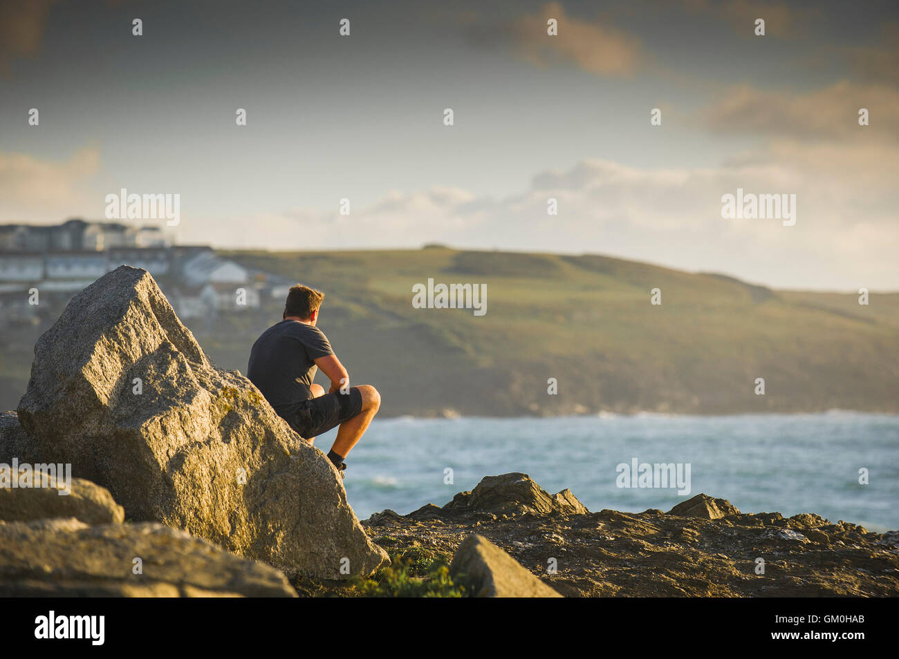 Ein Mann sitzt auf einem Felsen über dem Meer an Towan Landzunge in Newquay, Cornwall. Stockfoto