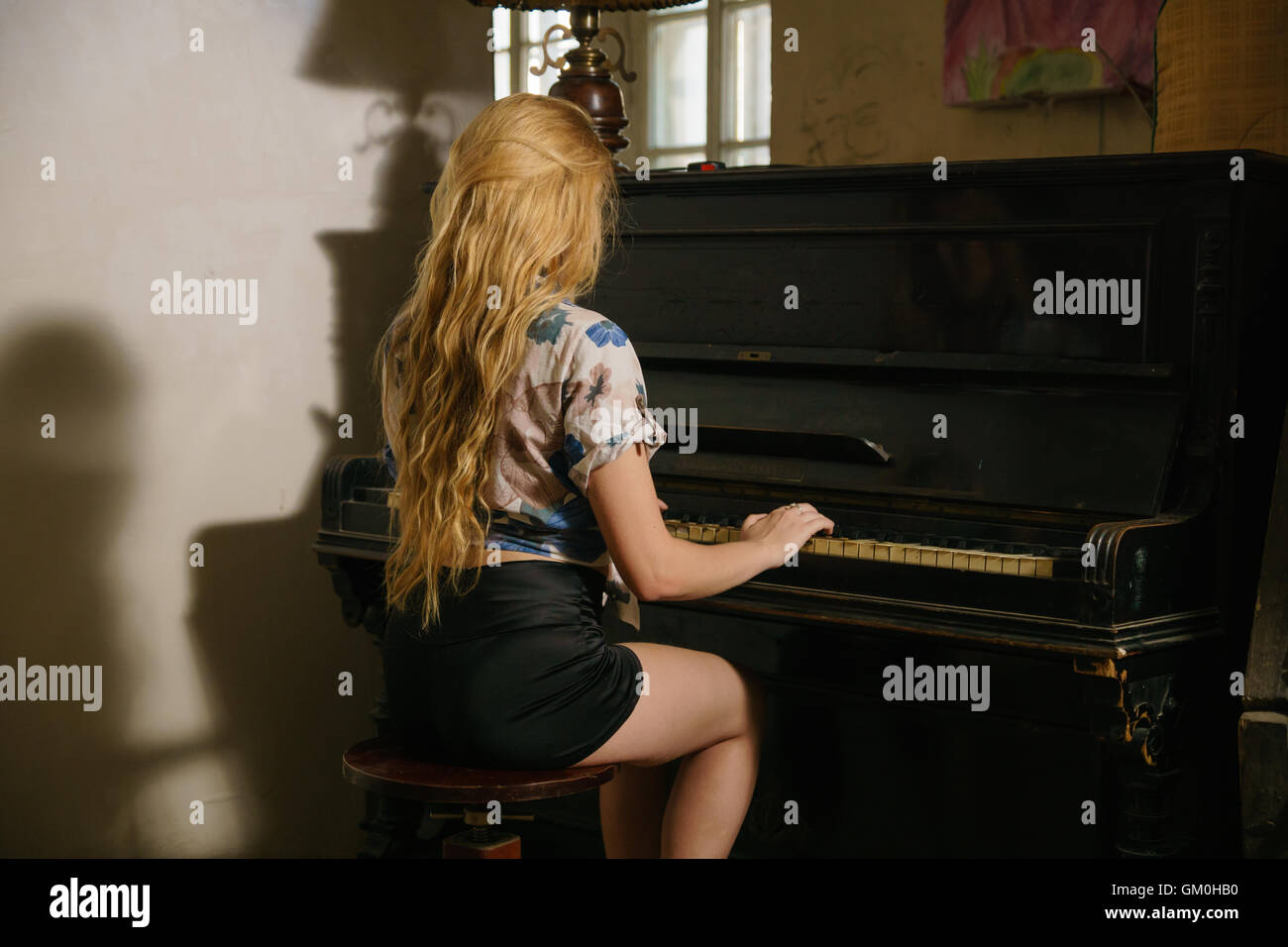 schönes blondes Mädchen mit offenen Haaren spielt auf dem Klavier sitzen auf dem Stuhl Stockfoto